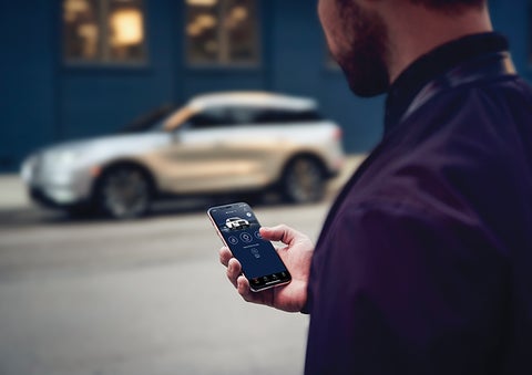 A person is shown interacting with a smartphone to connect to a Lincoln vehicle across the street. | White's Canyon Motors - Lincoln in Spearfish SD