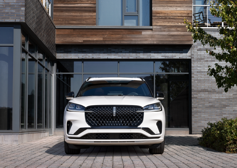 A white 2025 Lincoln Aviator® SUV is shown parked outside a modern building with gray brick and wood accents. | White's Canyon Motors - Lincoln in Spearfish SD