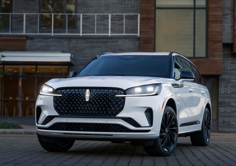 A white 2025 Lincoln Aviator® SUV is shown parked outside a modern building with gray brick and wood accents. | White's Canyon Motors - Lincoln in Spearfish SD