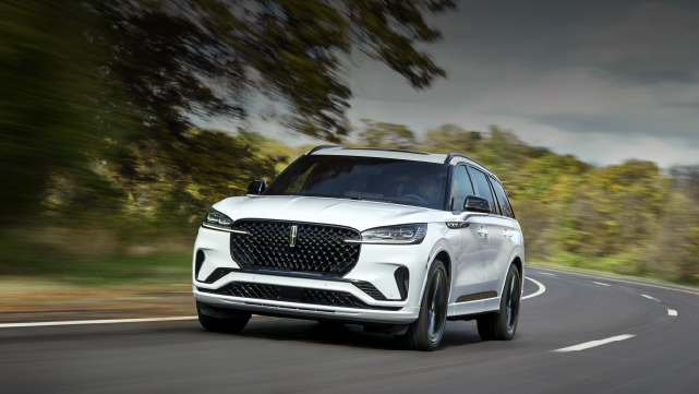 A white 2025 Lincoln Aviator® SUV is being driven down a road lined with trees. | White's Canyon Motors - Lincoln in Spearfish SD