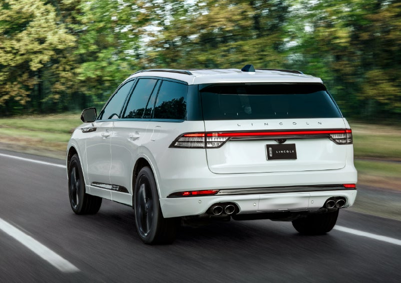 A white 2026 Lincoln Aviator® SUV is being driven away down a road lined with colorful trees. | White's Canyon Motors - Lincoln in Spearfish SD