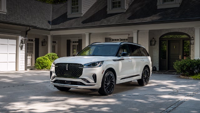 A white 2026 Lincoln Aviator® SUV is parked in the driveway of a luxury home. | White's Canyon Motors - Lincoln in Spearfish SD