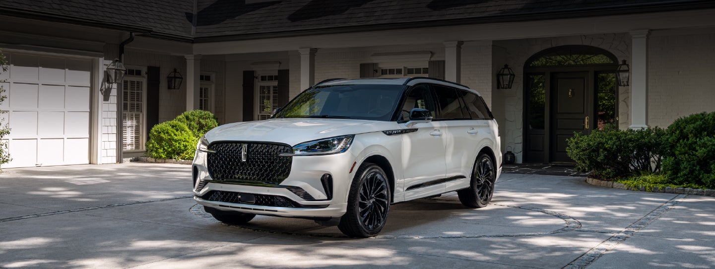 A white 2026 Lincoln Aviator® SUV is parked in the driveway of a luxury home. | White's Canyon Motors - Lincoln in Spearfish SD