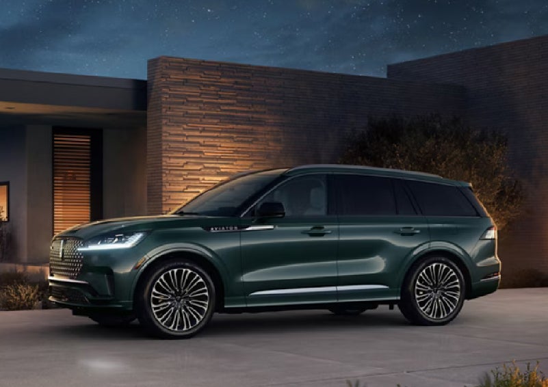 A green 2027 Lincoln Aviator® SUV is parked outside a contemporary home. | White's Canyon Motors - Lincoln in Spearfish SD