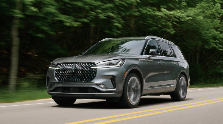 A 2027 Lincoln Aviator® SUV is being driven down a road lined with trees. | White's Canyon Motors - Lincoln in Spearfish SD