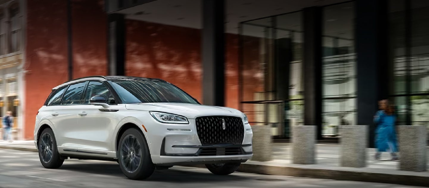 The 2024 Lincoln Corsair® SUV with the Jet Appearance Package and a Pristine White exterior is being driven down a city street.